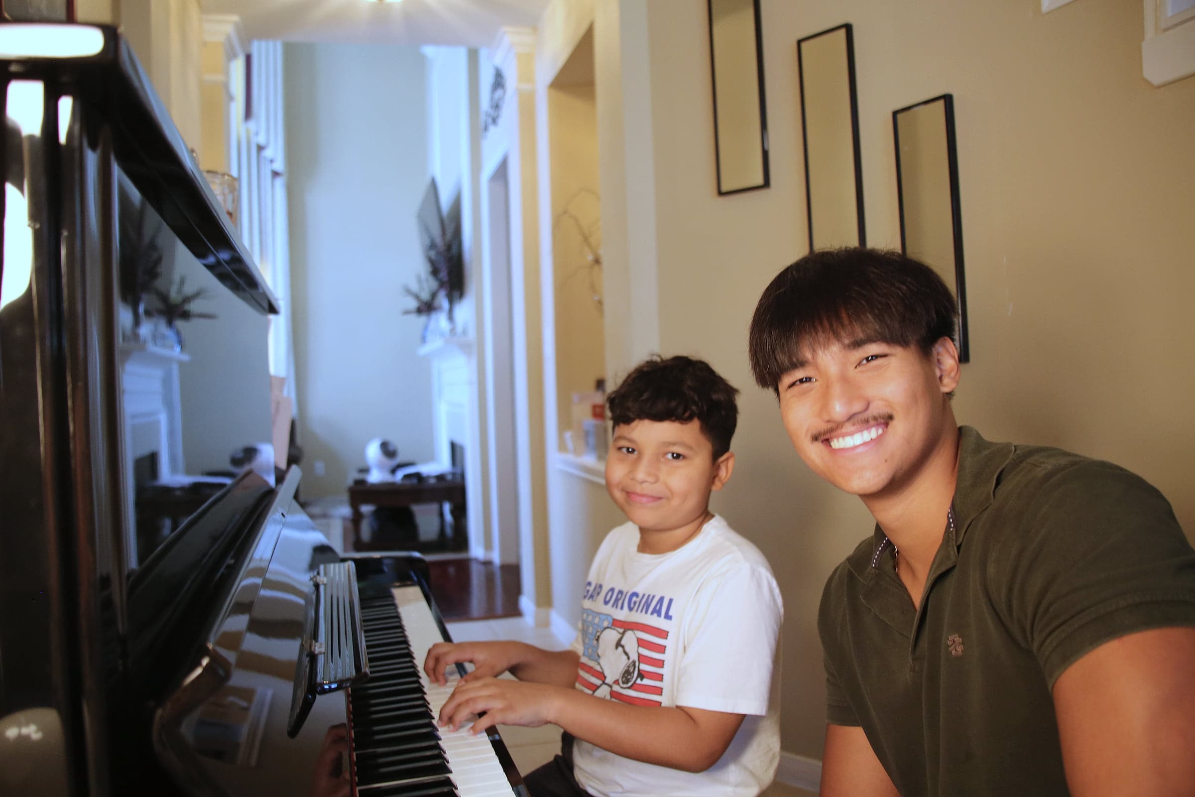 Preston at an upright piano beside a young student, both turning to smile at the camera