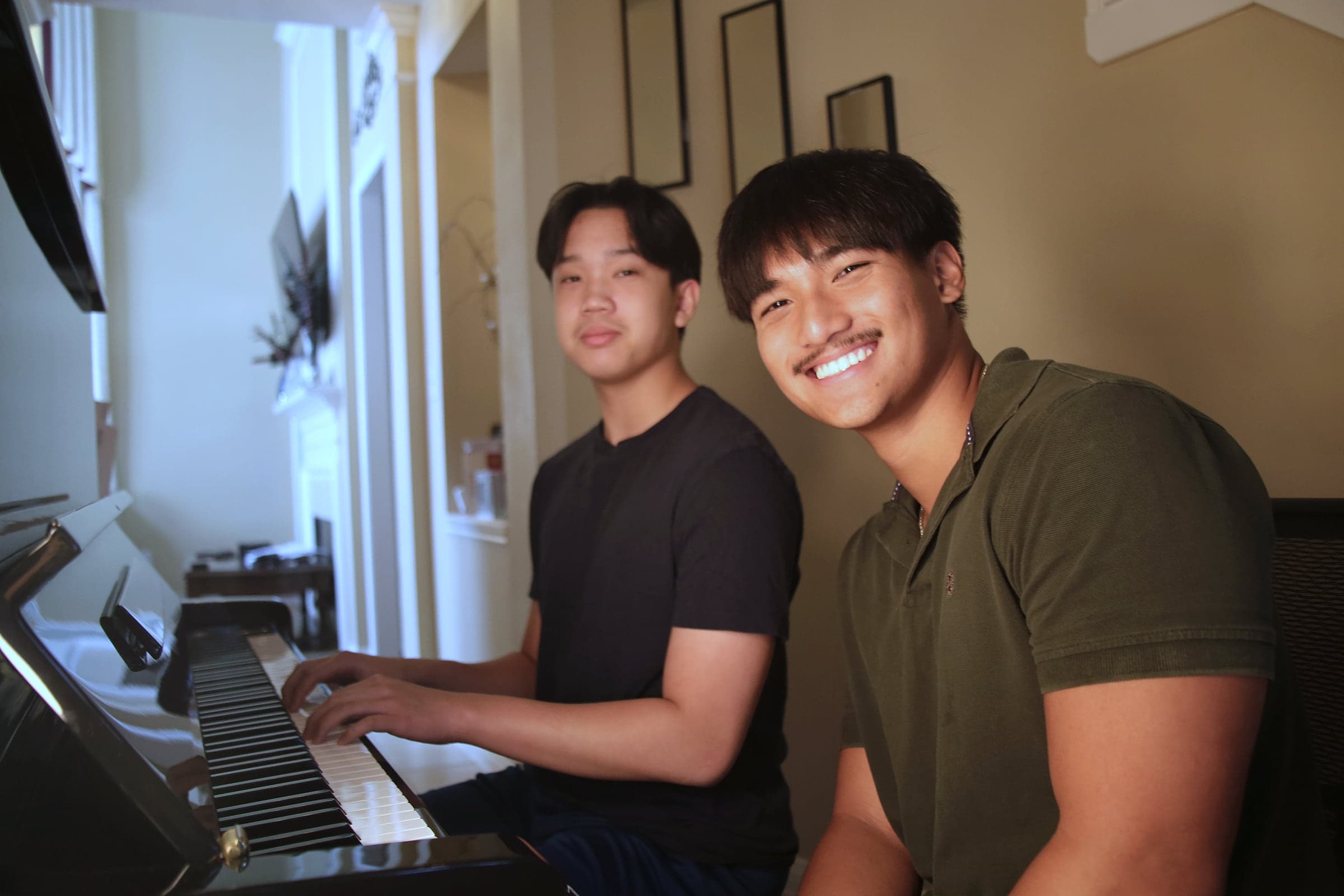 Preston playing an upright piano alongside a student