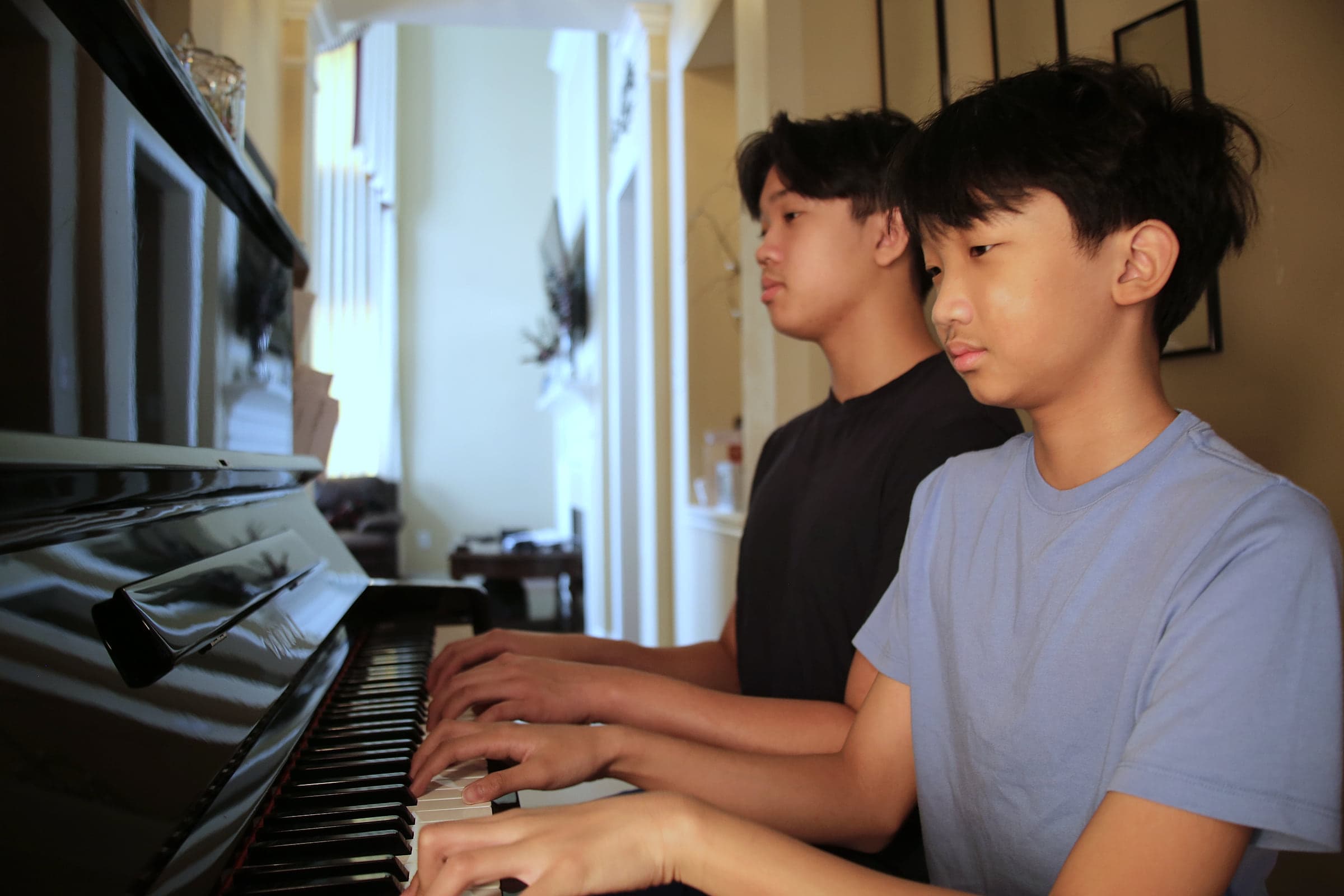 Two students side by side at the piano, concentrating on the keys